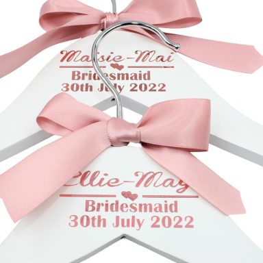 Bridesmaid Hangers Personalised white wooden hangers with pink bows, labelled for bridesmaids' dresses.